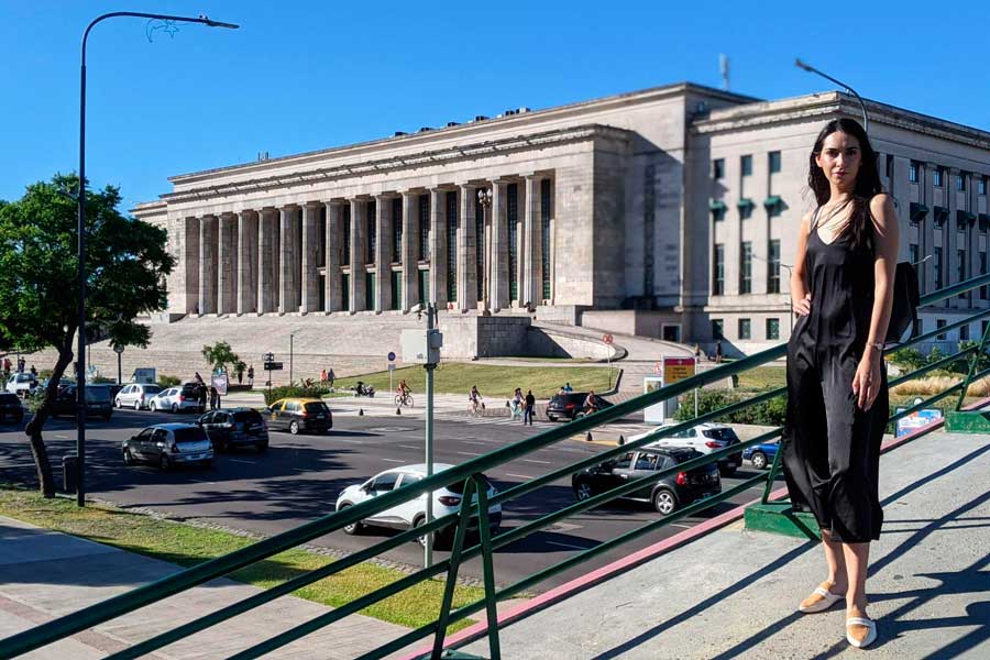 Clara posing for a photo under the clear blue sky with the Facultad de Derecho on her background