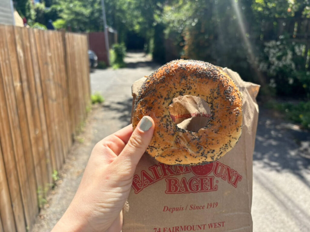 The author's hand holding a bagel from Fairmount Bagel shop