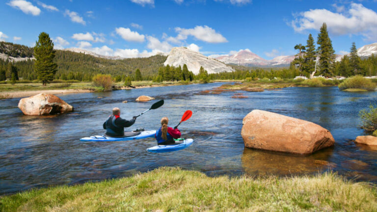 A father and daughter kayaking with mountains views in the background