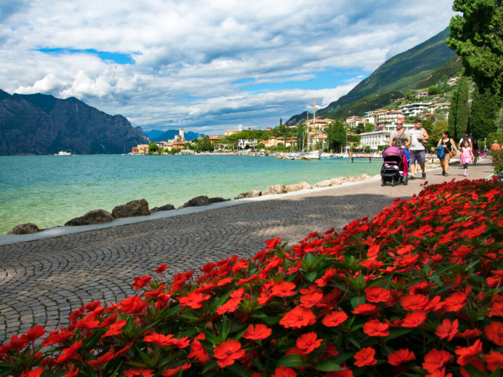 View of the blooming flowers and a family walking along Lake Garda with the cityscape in the background