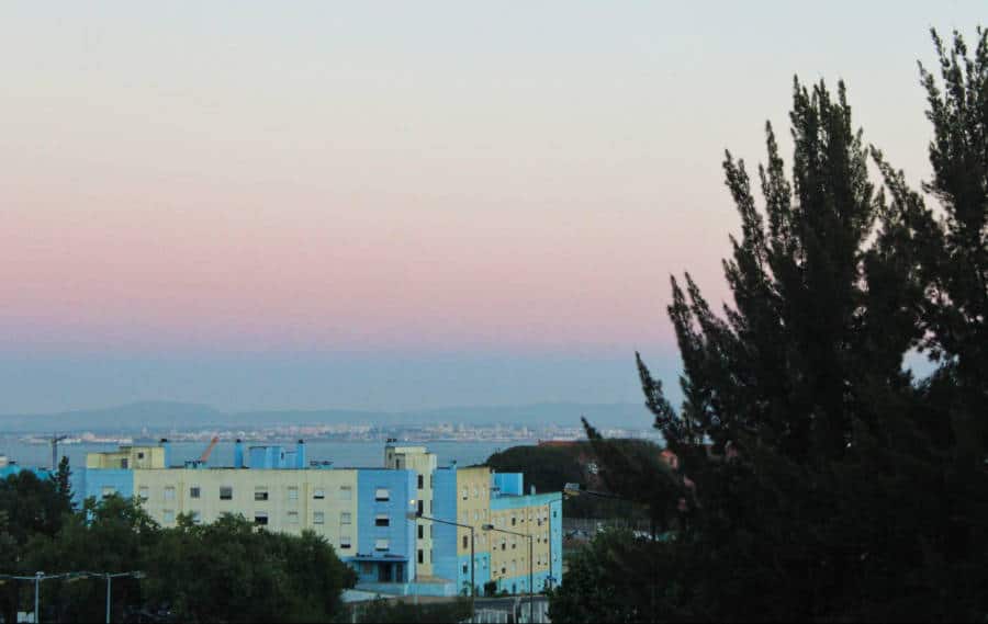 A blue and white building from a distance with a scenic view in the background during sunrise