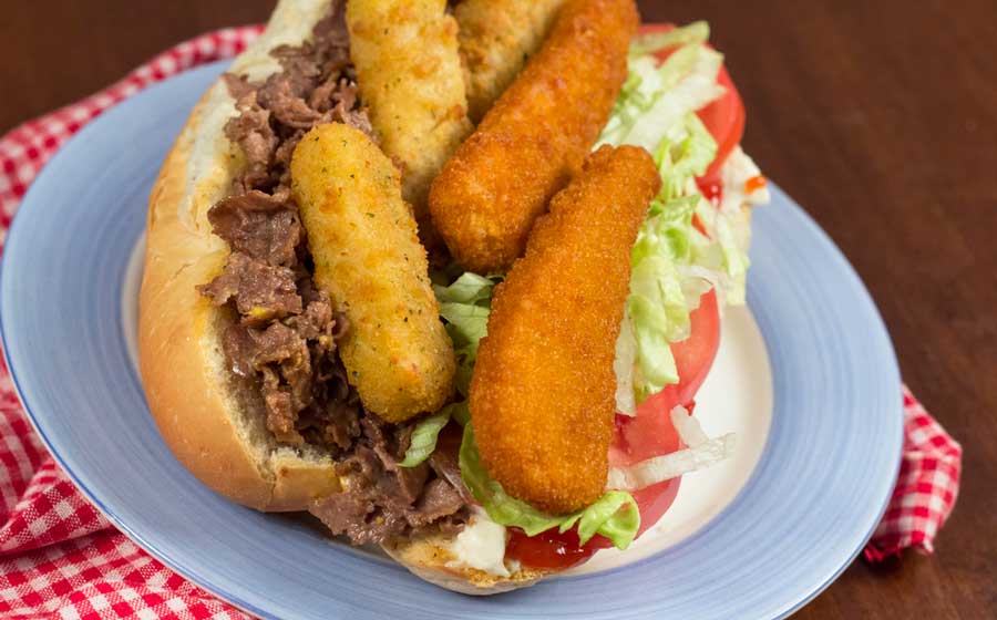 A fat sandwich loaded with chicken strips, mozzarella sticks, and fries on a plate