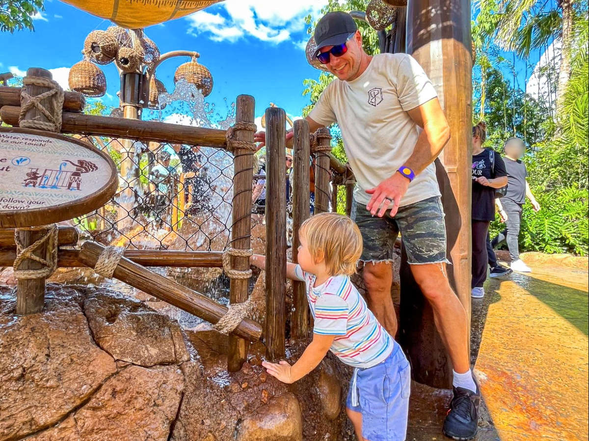 A father looking at his son enjoying the water at the Journey of Water 