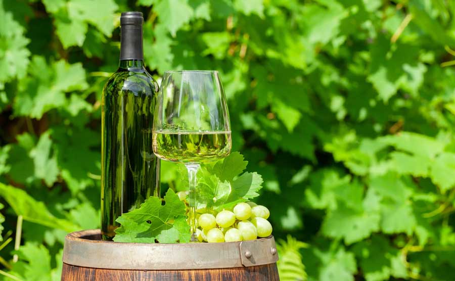 A bottle of wine, a glass of wine, and grapes on top of a wine barrel