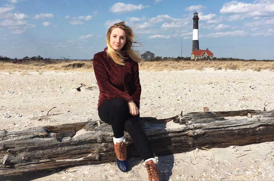 The author sitting on a tree trunk with the Fire Island Lighthouse on her background
