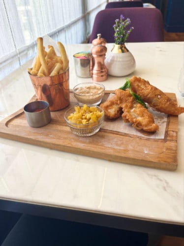 A serving of fish and chips with dipping sauces on a wooden board at Blue Aster