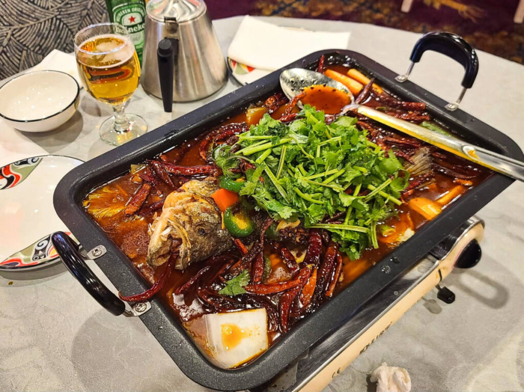 A pan with a whole fish served with vegetables in a broth of spices