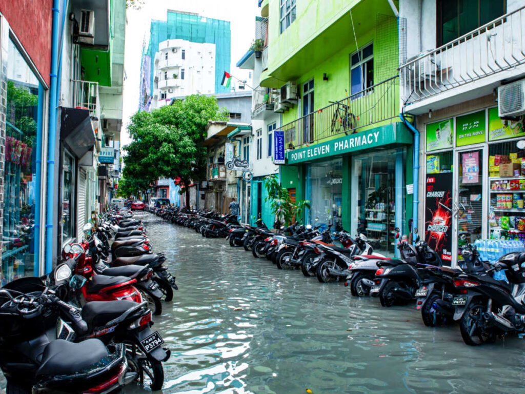 View of the flood in the street of Maldives with parked motorcycles outside the buildings