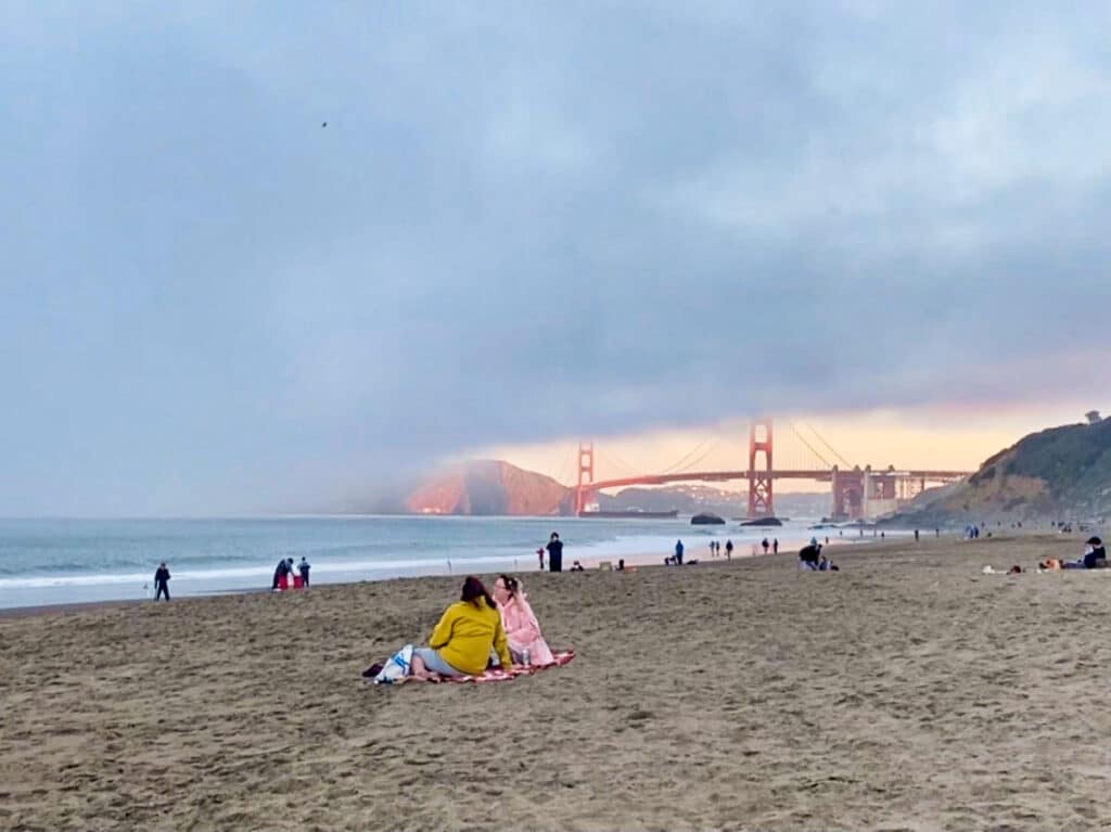 View of the people lounging at the shoreline with a fog over the Golden Gate Bridge in the background