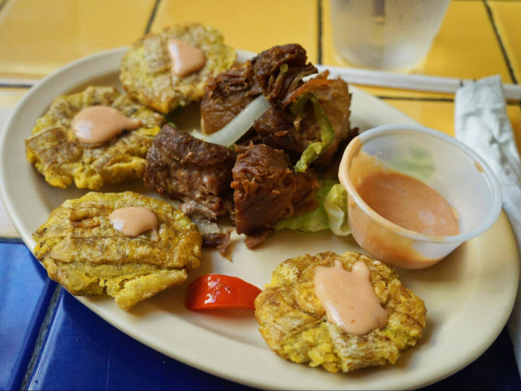 Roasted pork and tostones on a plate with a dip at El Patio