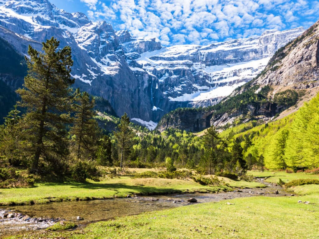 Picturesque view of the lush green landscape of French Pyrenees Mountains with the snowy mountains and cloudy sky in the background