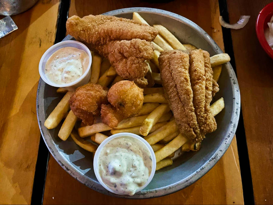 A plate full of fries topped with fried catfish and dipping sauces