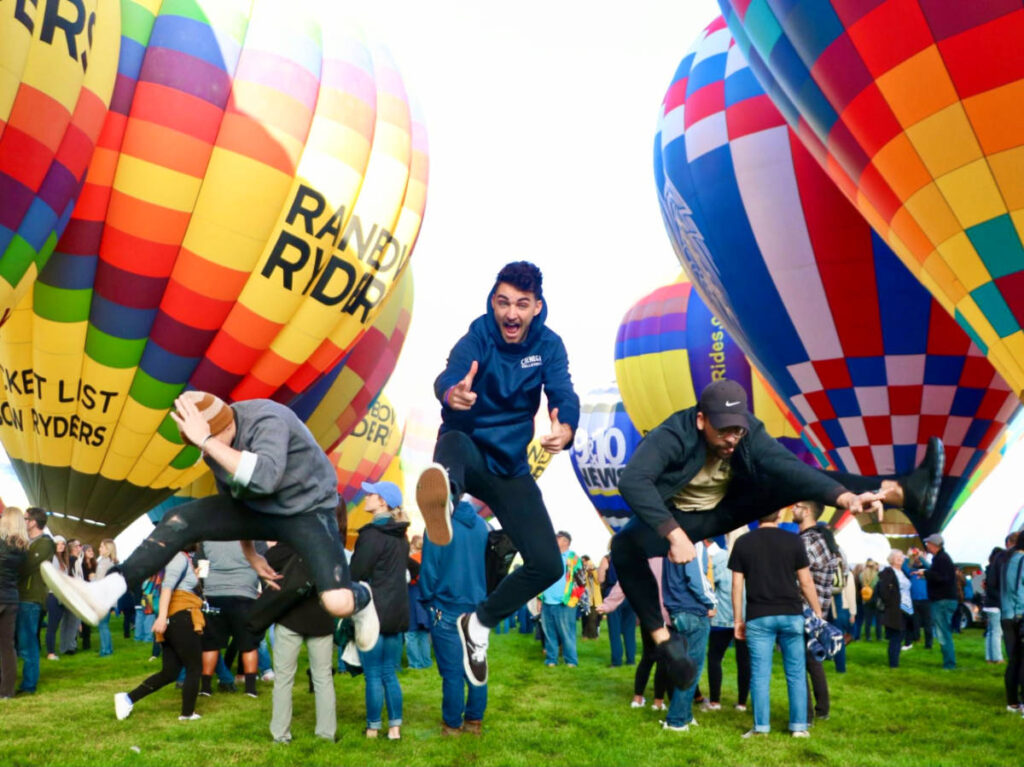 Men jumping with the hot air balloons in the background at the Rainbow Ryders Balloons