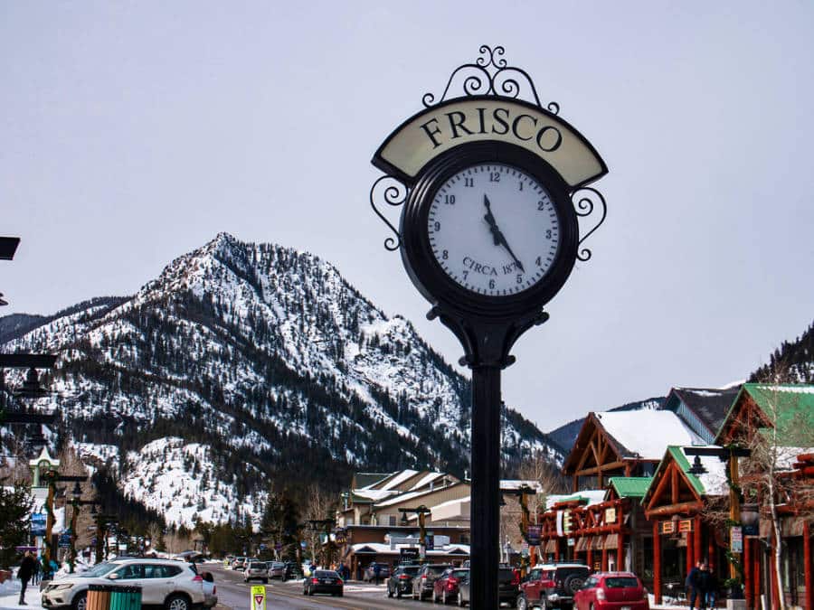 A closeup look of the town clock with a mountain view in the background of Frisco