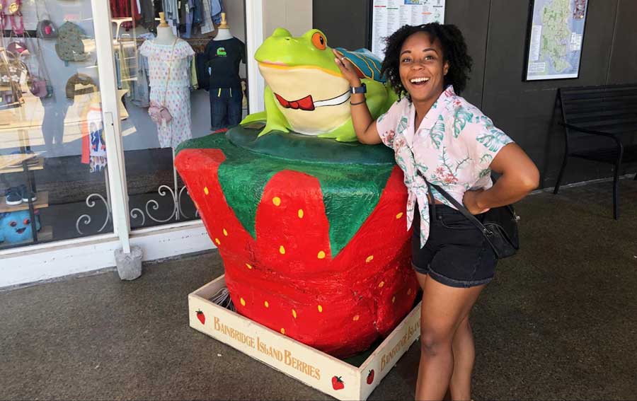 The author smiling for a photo with a frog sculpture in Bainbridge Island