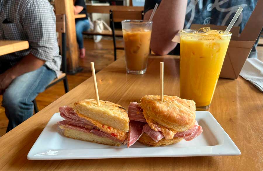 A ham and pimento cheese biscuits on a plate and a glass of juice in Frothy Monkey