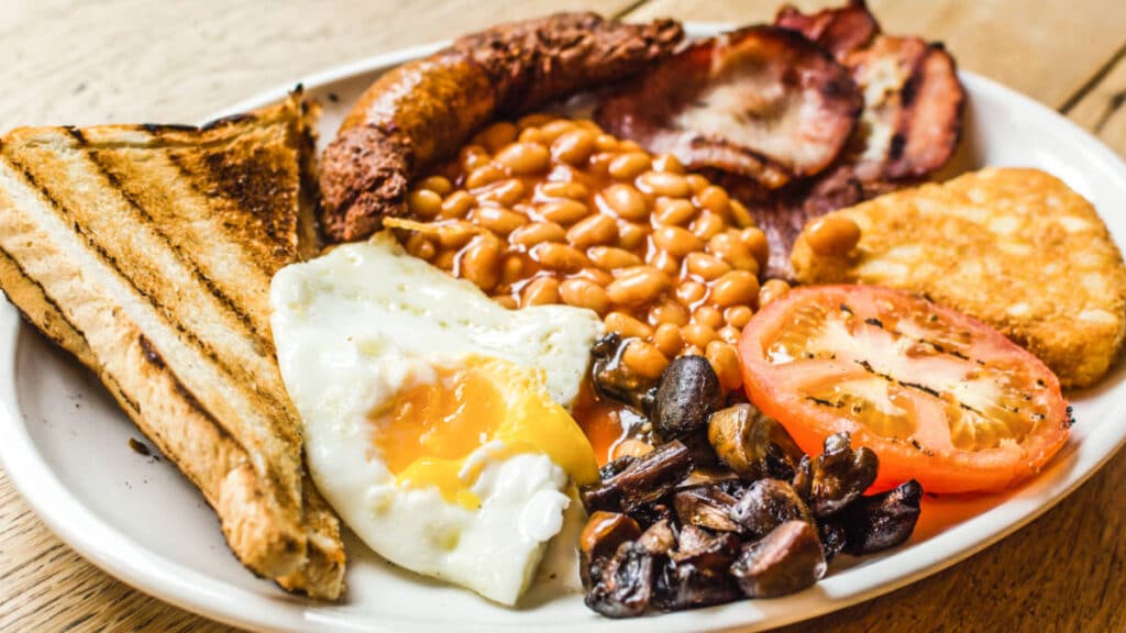 A big plate of Full English Breakfast including sausages, grilled tomatoes and mushrooms, egg, bacon, baked beans and toasted bread