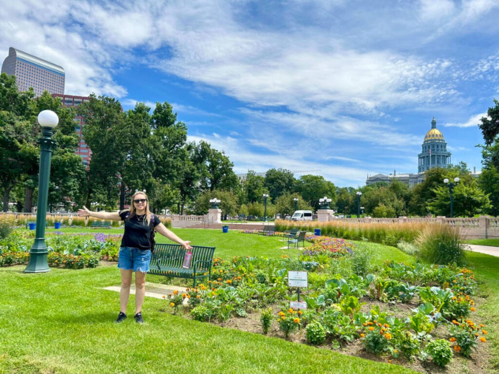 Author Laura Falin standing in front of a garden with a building in the background at Civic Center Park