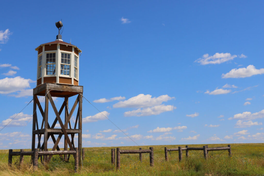 The guard tower at Amache National Historic Park against a grass plain and blue sky with clouds