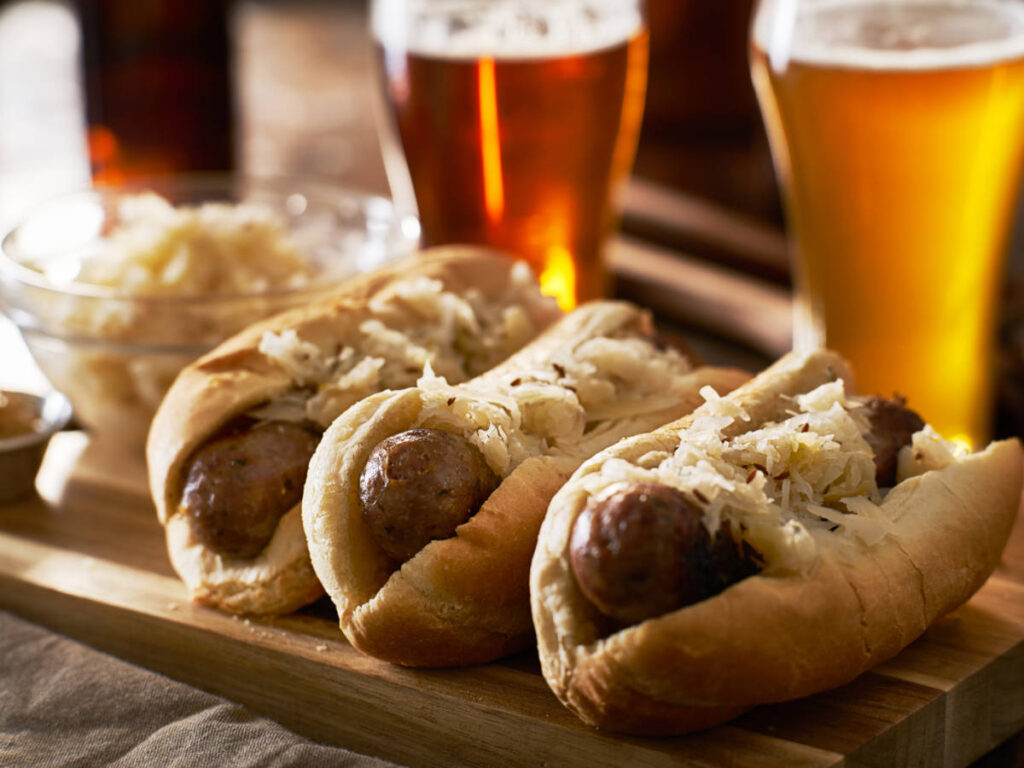 Three bratwursts with sauerkraut on a wooden board and glasses of beer