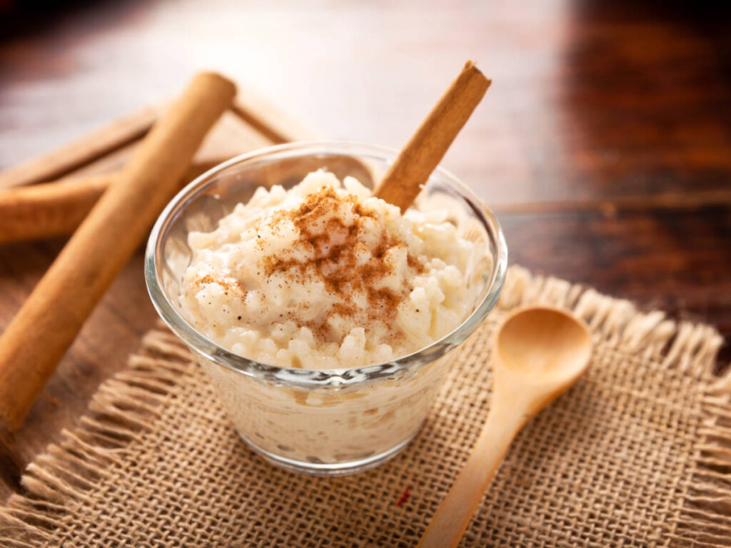 A glass of rice pudding topped with cinnamon powder and stick