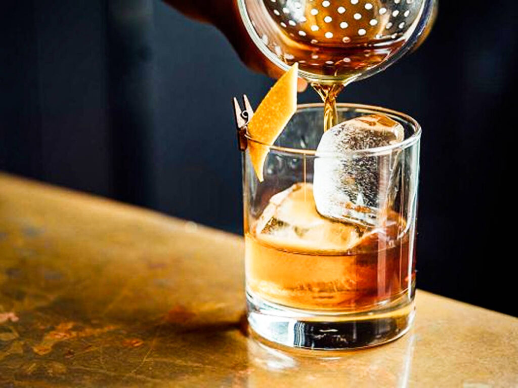 A glass of rum pouring on another glass with ice cubes