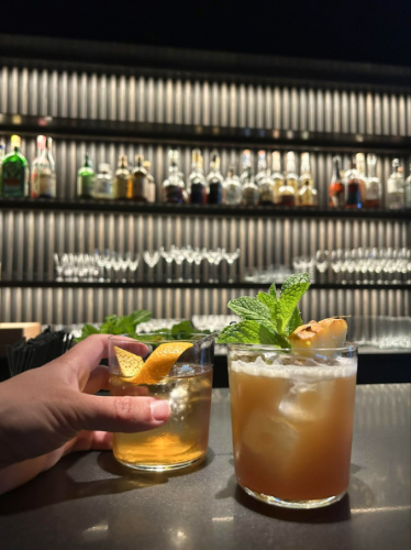 A hand holding a glass of cocktail on the bar counter