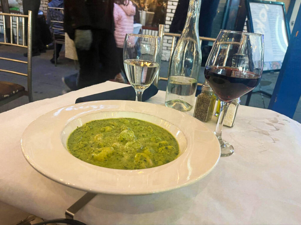 A deep plate with gnocchi and pesto paired with a Pinot Noir on the side