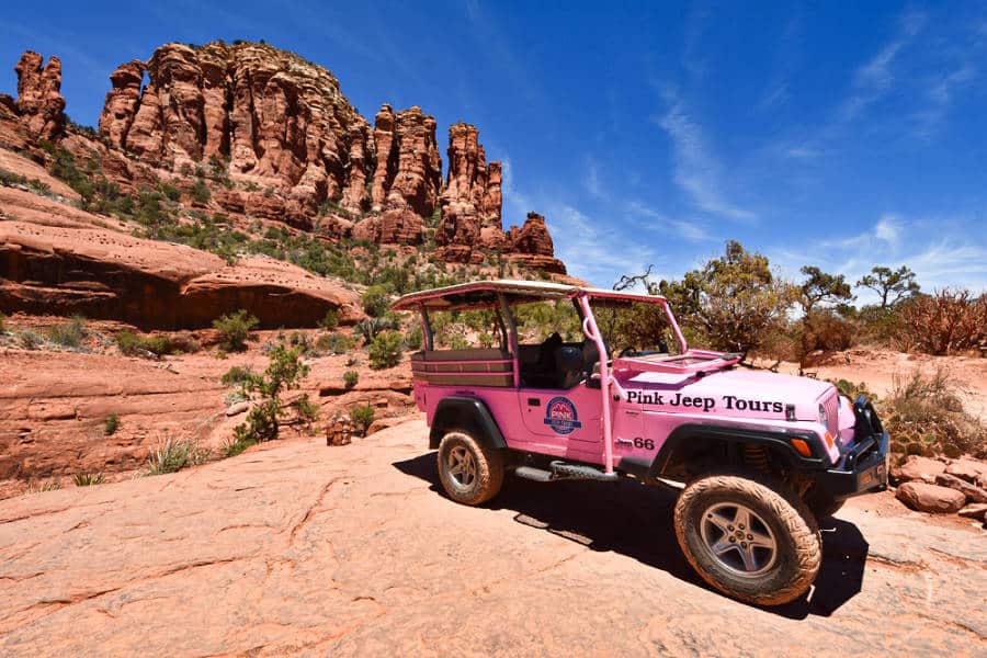 A pink jeep parked below the majestic rock mountains