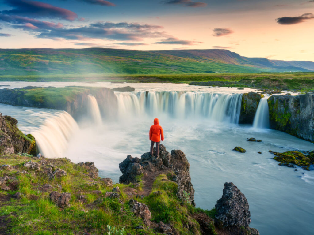A man stands on rocks enjoying the majestic views of Godafoss waterfall