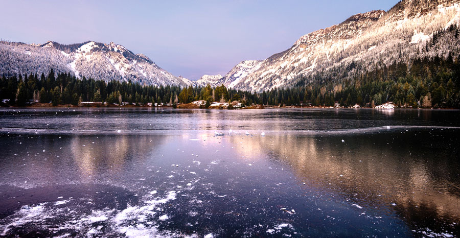 View of the Gold Creek Pond  surrounded by rocky mountains with snow