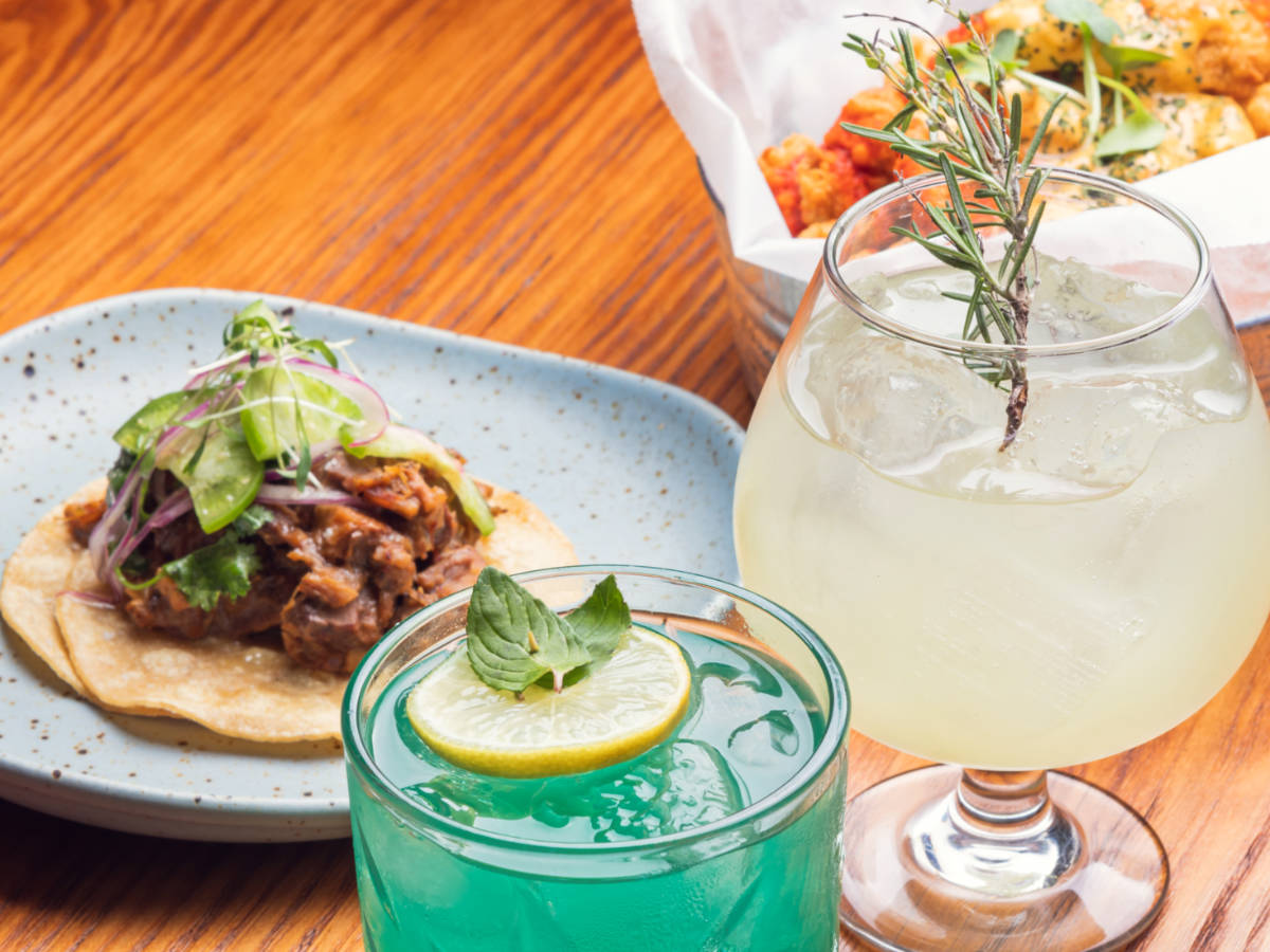 A plate of beef tacos and other Mexican food with glasses of gin tonics on the wooden table