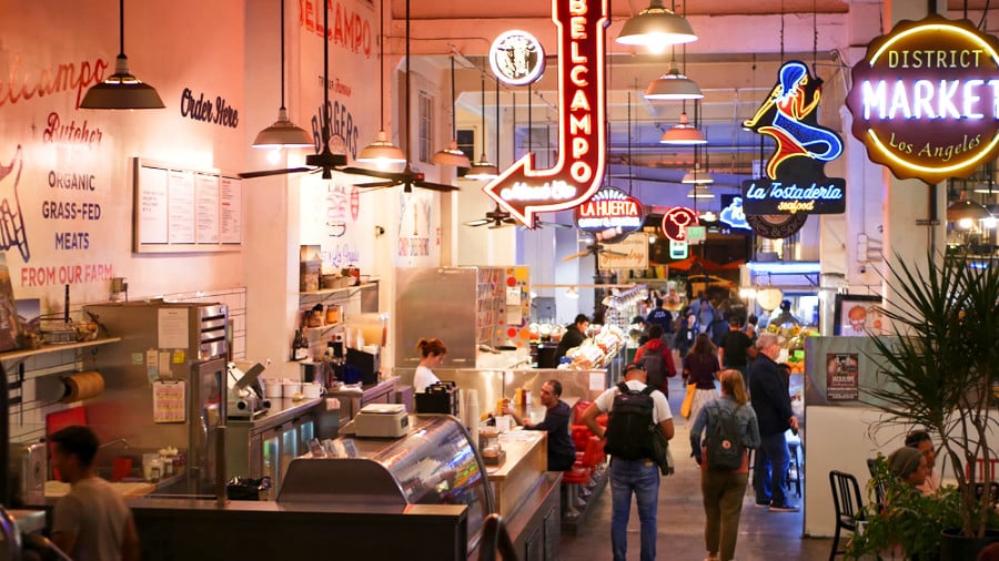 People walking pass the shops with retro neon signs above in Grand Central Market