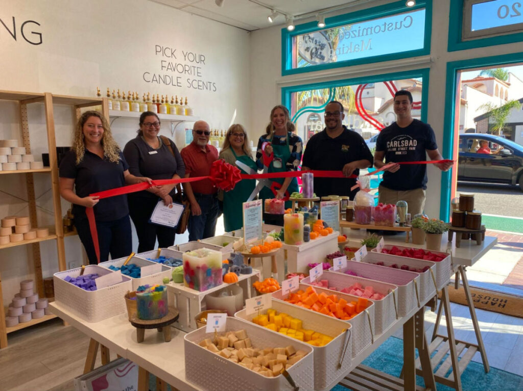 Author Jess and others hold a red ribbon to celebrate the grand opening of Candle Bar Carlsbad