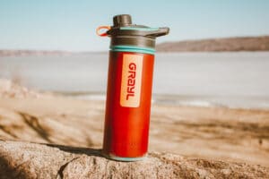A Grayl Water purifier sits on a rock in front of a beach and a frozen-over lake