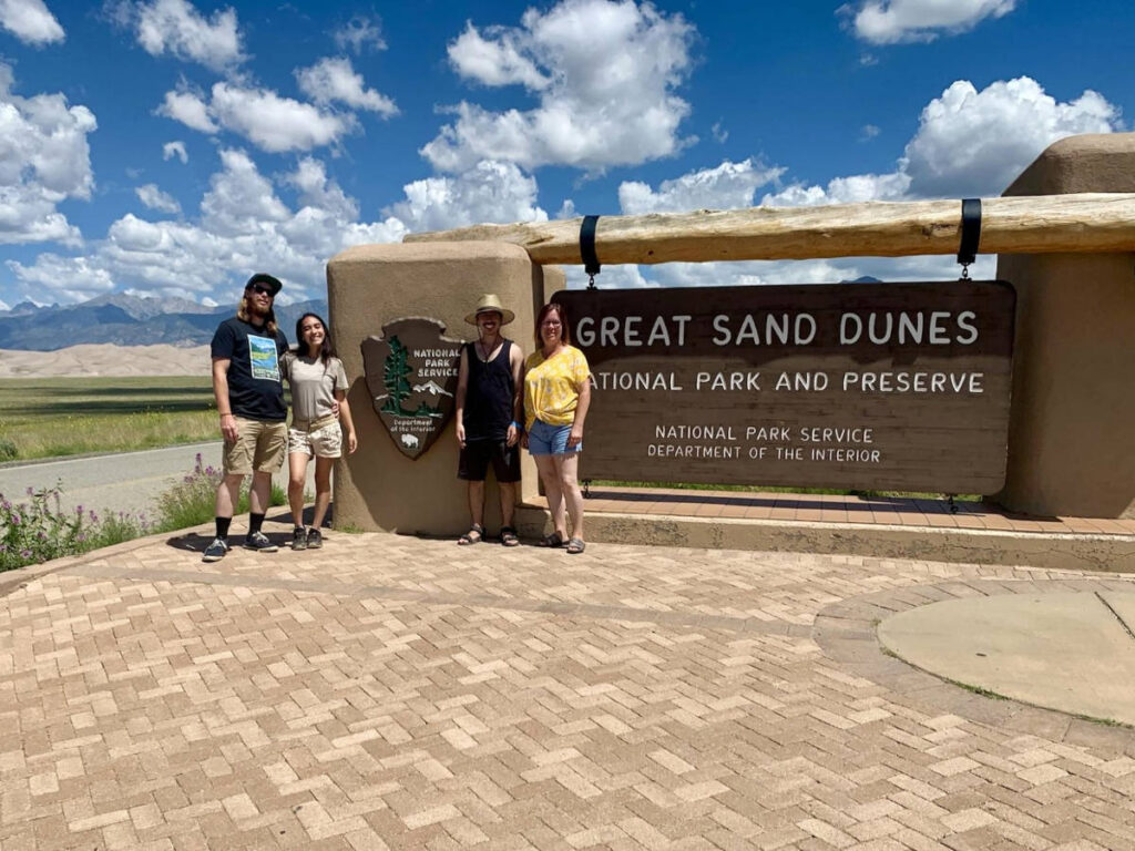 Travel Lemming editor, Abigail Bliss with her family smiling for a photo with the Great Sand Dunes National Park and Preserve Signage