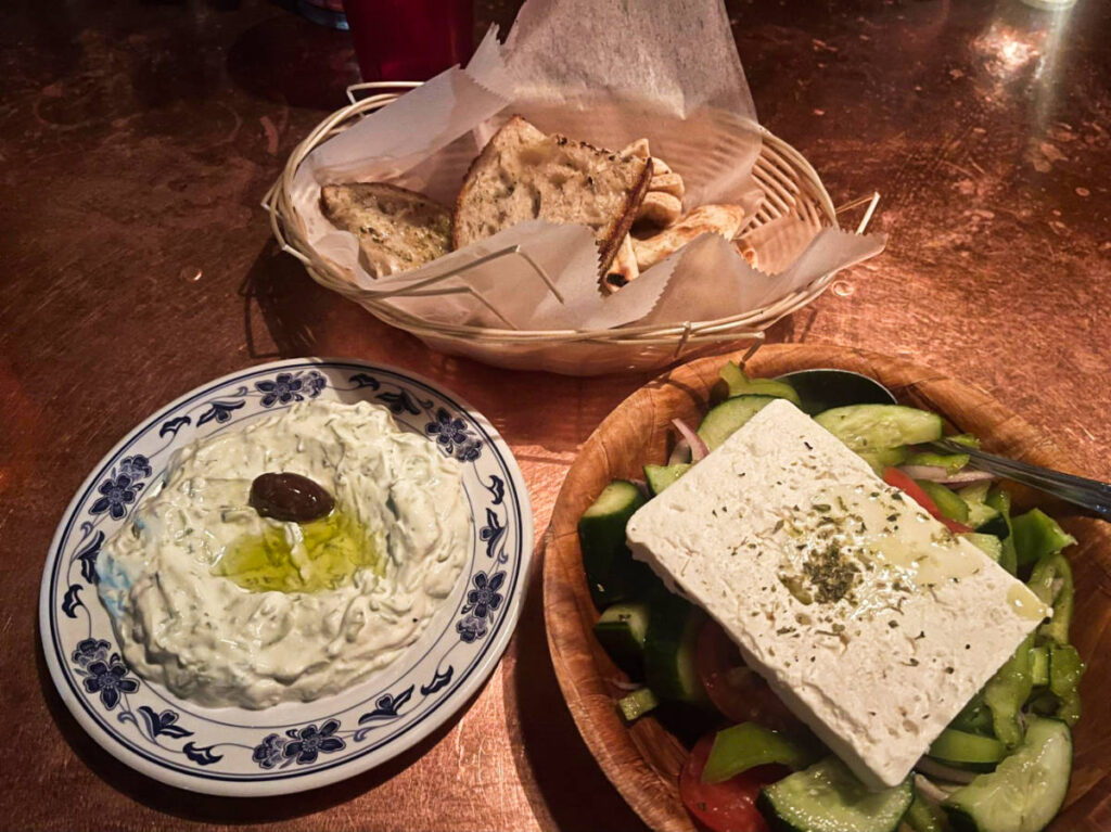 A bowl of Greek salad and pita on the basket with tzatziki on a plate at Kiki’s