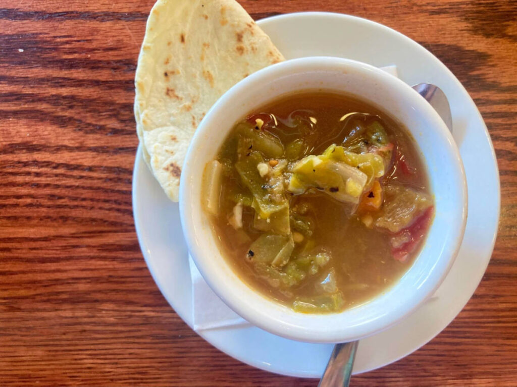 Closeup look of a bowl of green chile soup with pita bread on the side