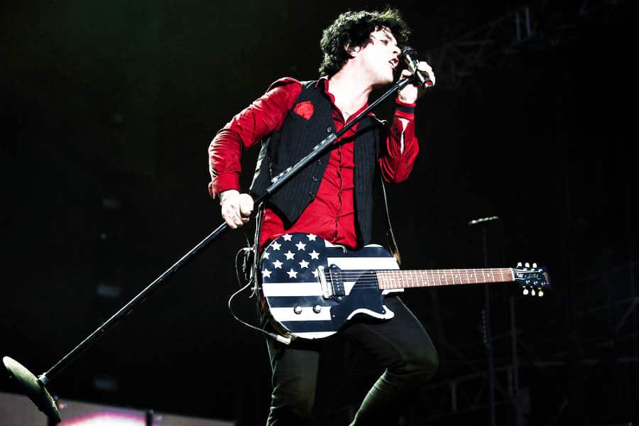 Green Day with a guitar and holding a mic while performing on stage