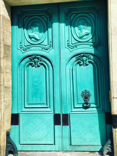 A turquoise door featuring two
decorative carvings, reminiscent of Parisian architecture