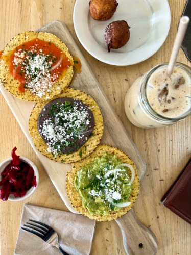 The Guatemalan tostadas, Ghanaian "puff puffs," and an oat milk cardamom latte on a wooden tabel