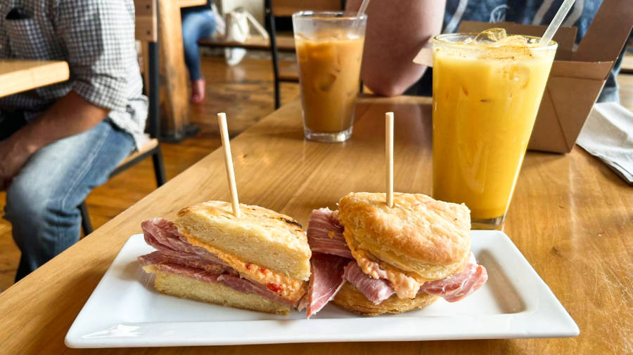 Two ham and pimento cheese biscuits on a plate with two glasses of drinks at Frothy Monkey