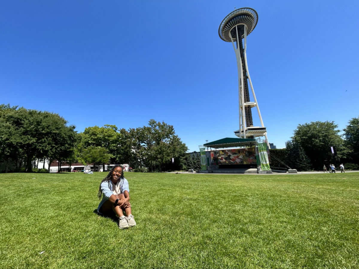 Author Chelsea Booker sitting on the grass in front of the Space Needle, enjoying her time at the Seattle Center