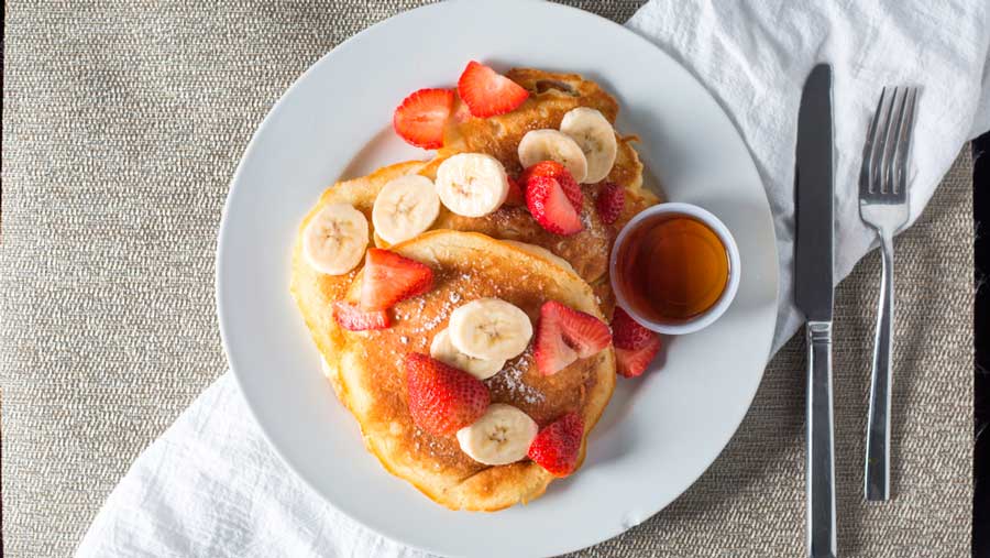 Pancakes with strawberries and bananas on top with maple syrup on side