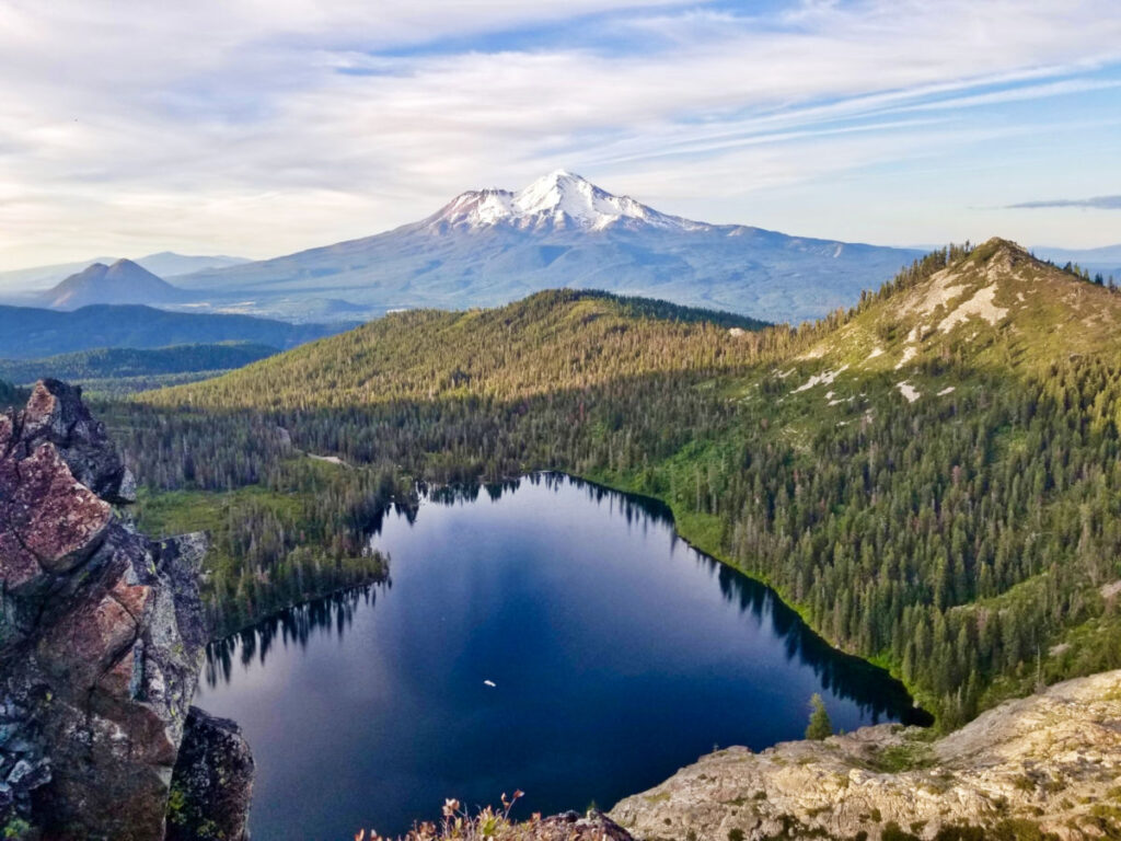 Aerial view of the heart shaped lake surrounded by the rainforest with the Mount Shasta in the background