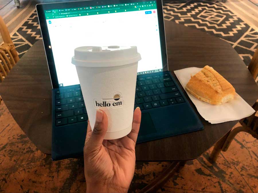 The author holding a cup of coffee with her laptop beside a bread on the background