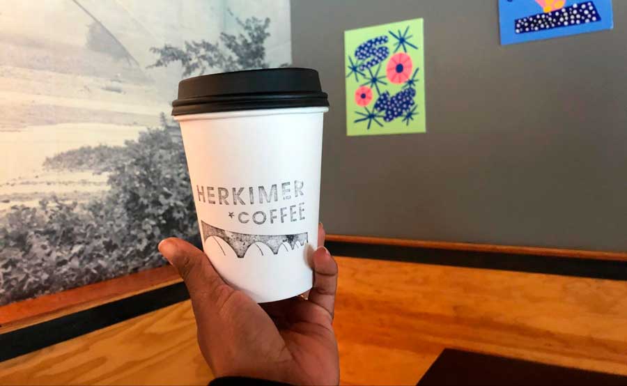The author holding a cup of coffee with art on the wall in Herkimer Coffee