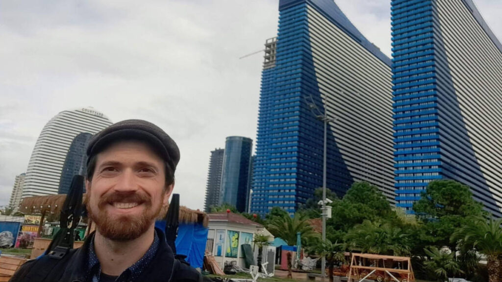 The author Matthew Reppond smiling for a selfie in front of buildings in Batumi