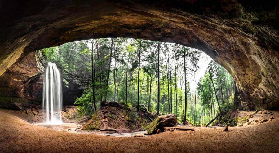 An enormous sandstone recess cave with a waterfall at the entrance