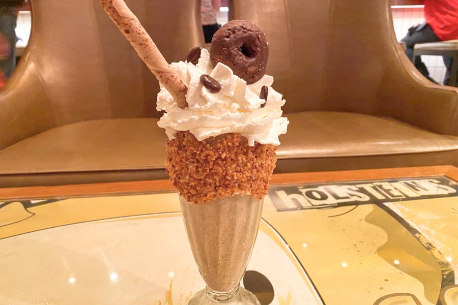 A tall glass of chocolate milkshake topped with cream, mini donut and a wafer roll in Holstein’s